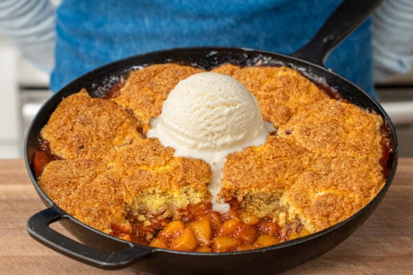 cast iron pan filled with peach cobbler topped with vanilla ice scoop