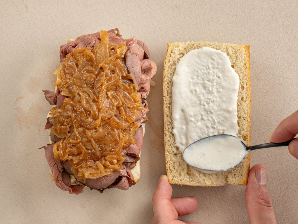 two sandwich halves one with beef and caramelized onions one with horseradish