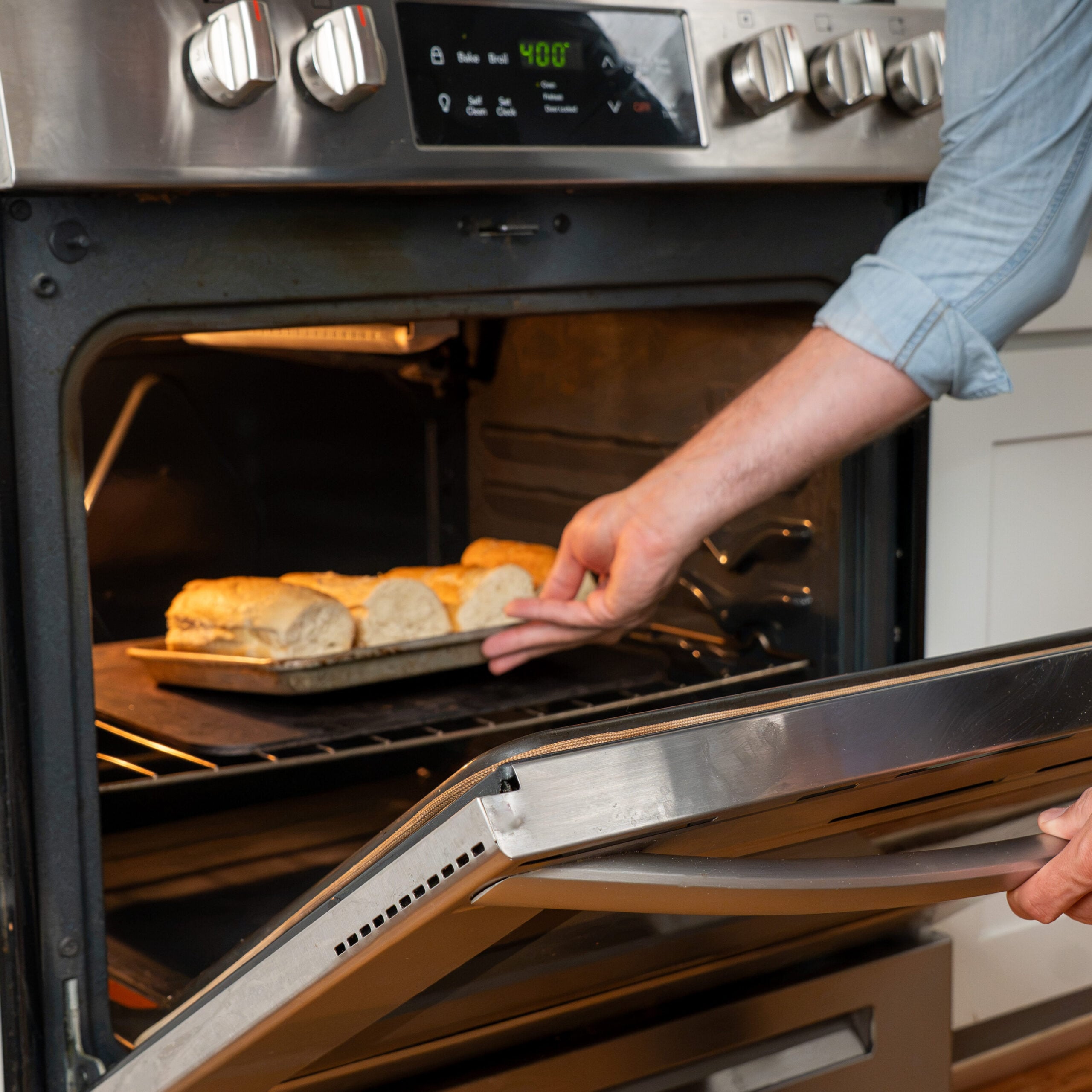 man sliding tray of baguettes into oven