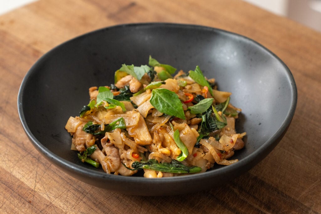 pad kee Mao drunken noodles with basil in black bowl on wood cutting board