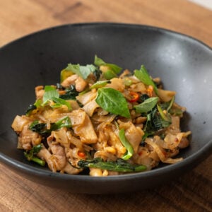 drunken noodles with basil in black bowl on wood cutting board