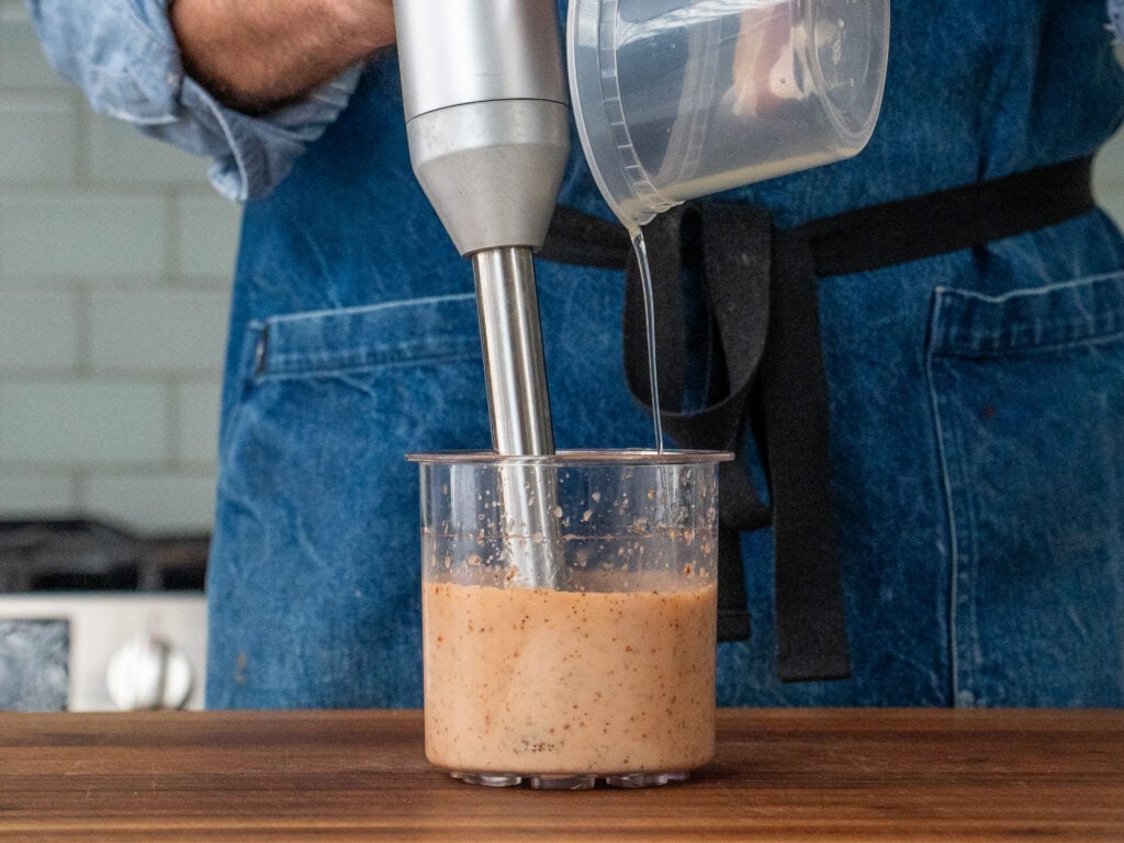 immersion blender blending oil into Italian dressing in clear container