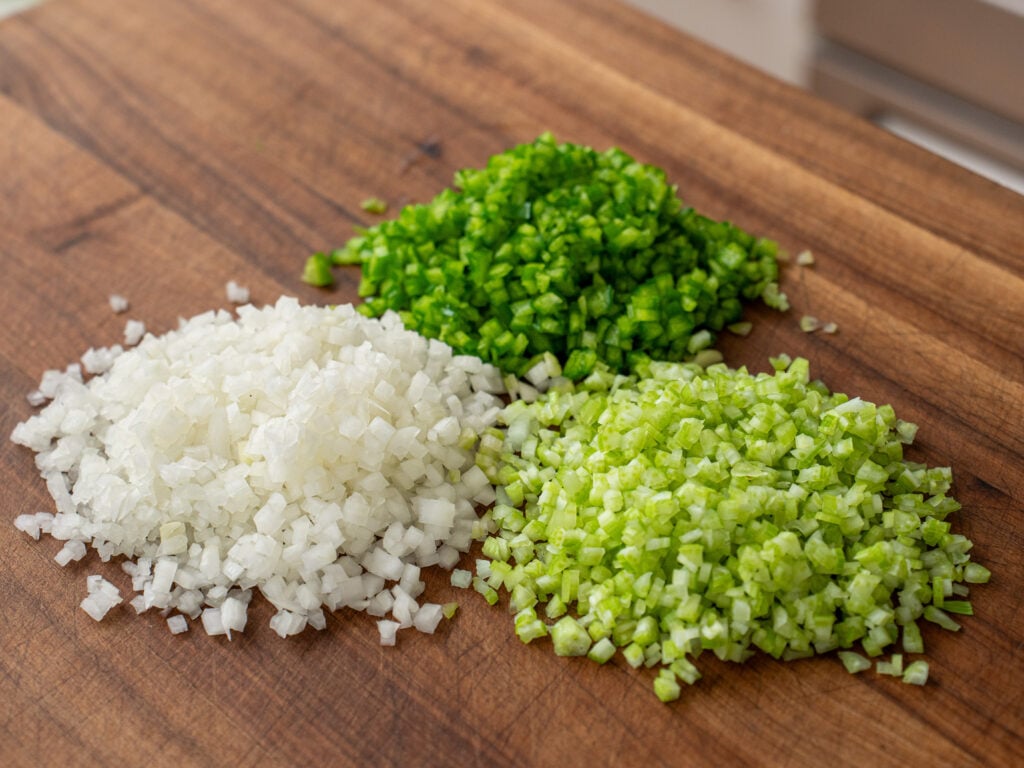 piles of diced onion celery and green pepper on wood cutting board