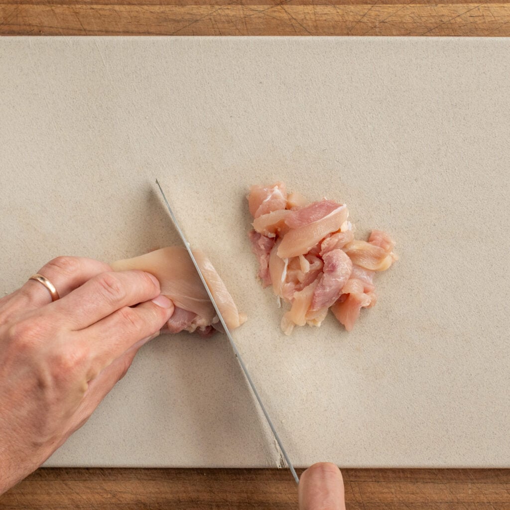 knife cutting chicken thigh into pieces on cutting board