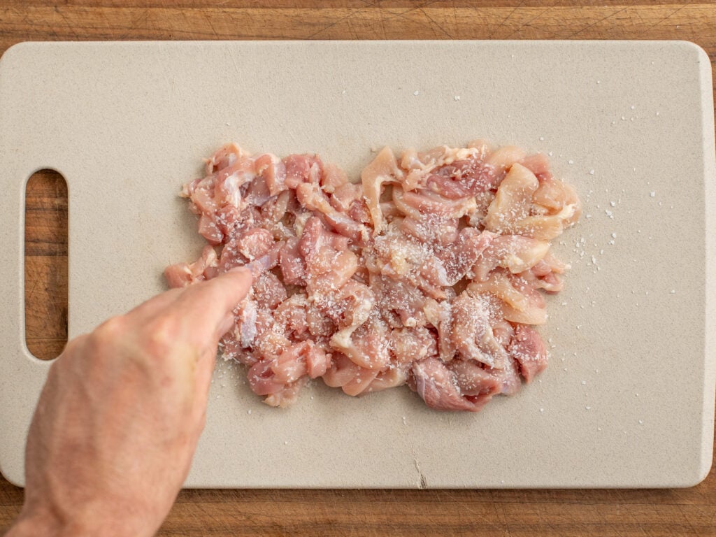 salting cut chicken thigh on cutting board