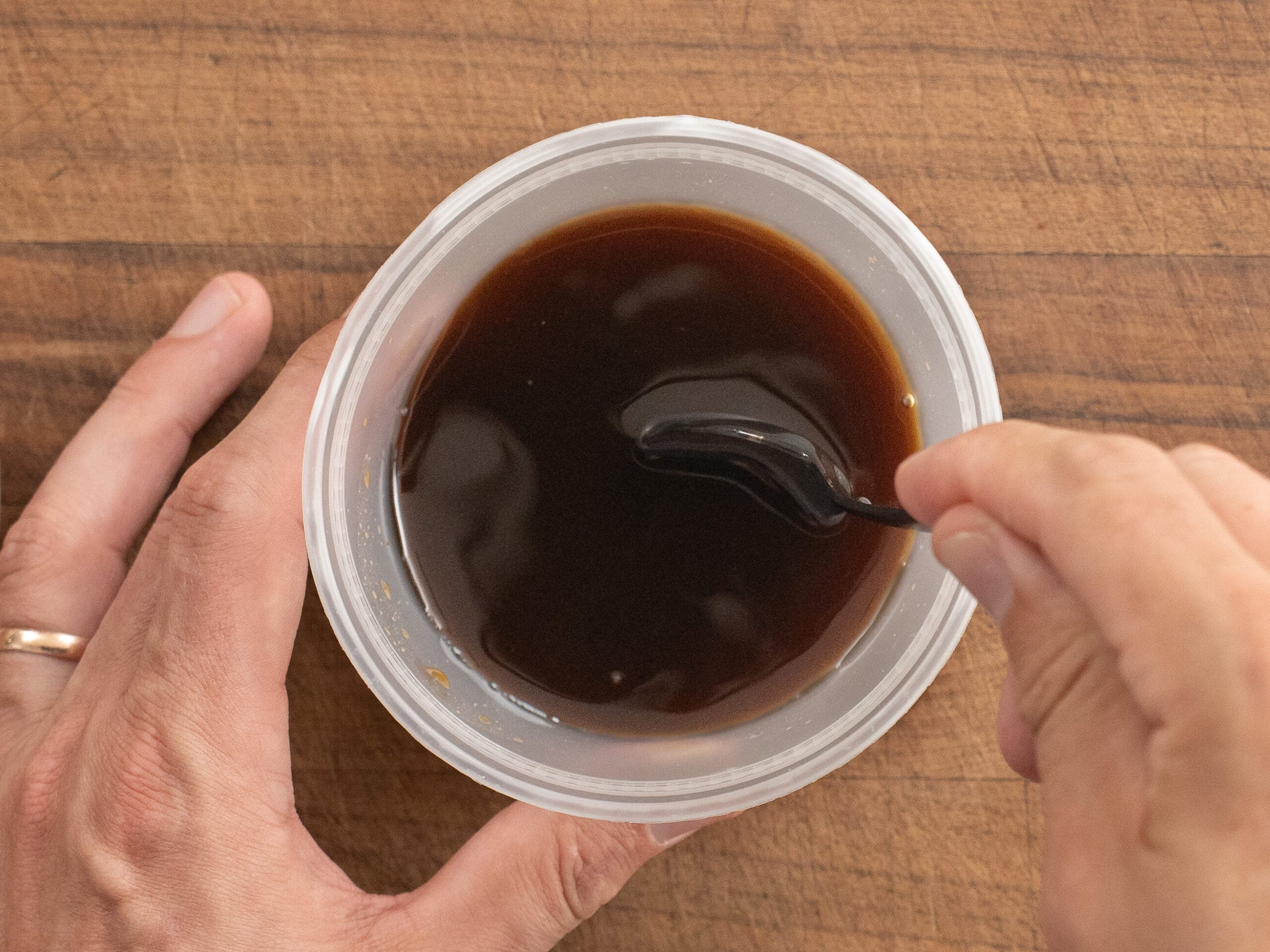 stirring container of brown liquid with black spoon