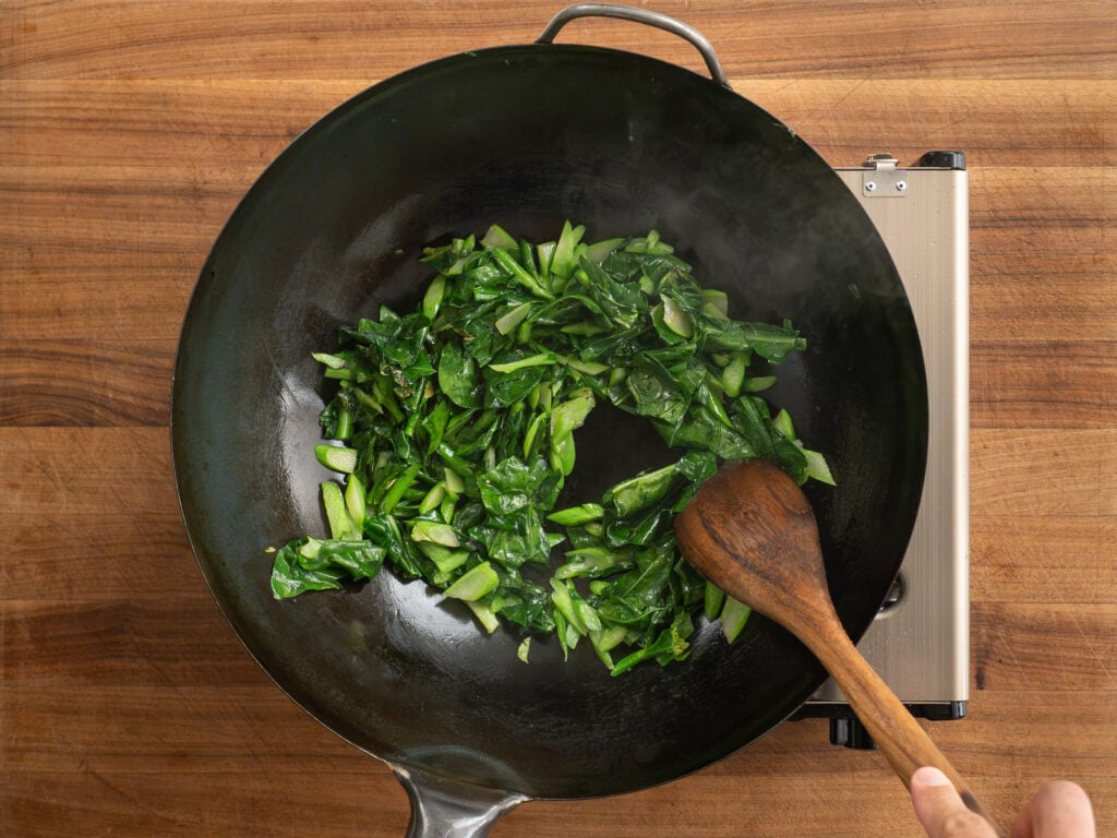 using wooden spoon to move around green vegetables in wok