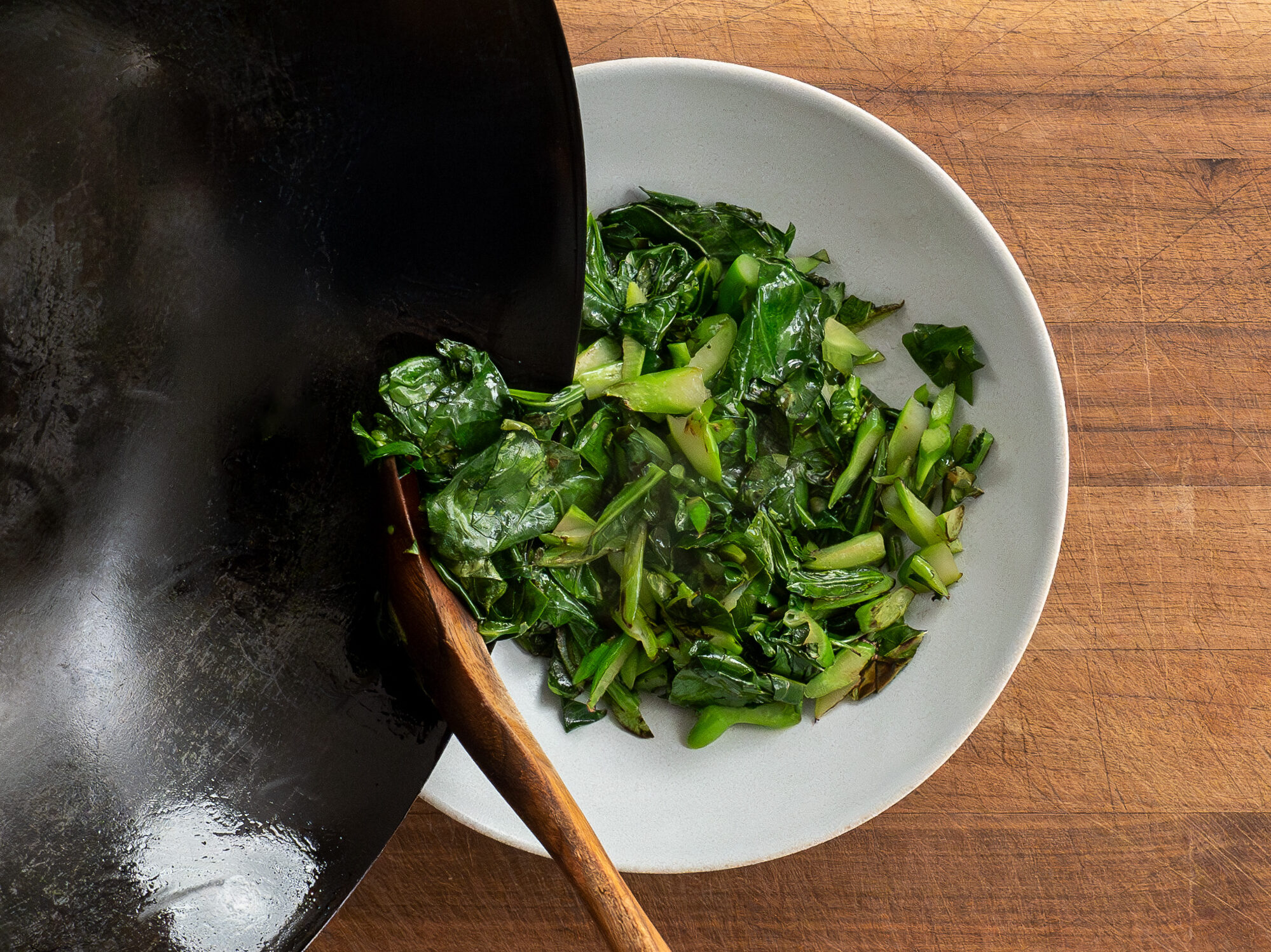 transferring cooked Chinese broccoli from wok into grey bowl
