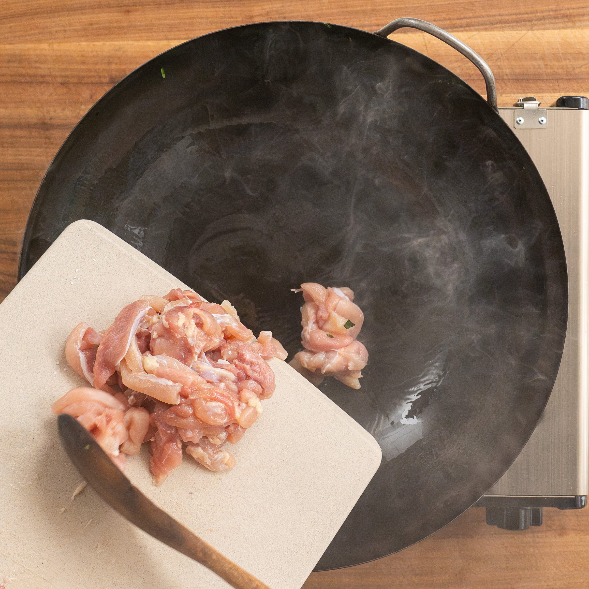 transferring cut chicken thigh pieces from cutting board into wok with wooden spoon