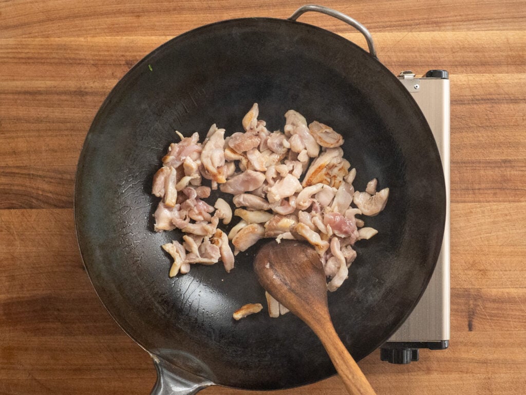 cooking chicken thigh pieces in wok with wooden spoon