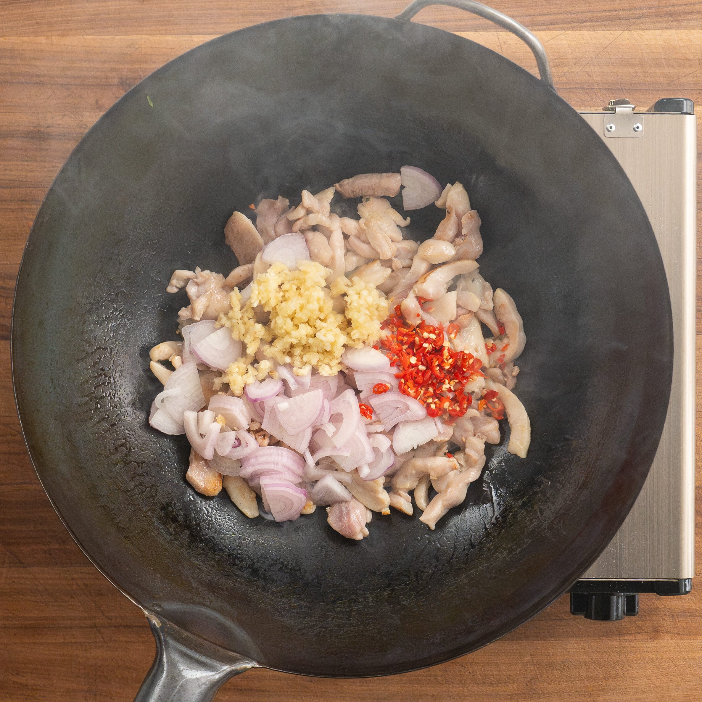 adding aromatics to chicken thigh pieces cooking in wok