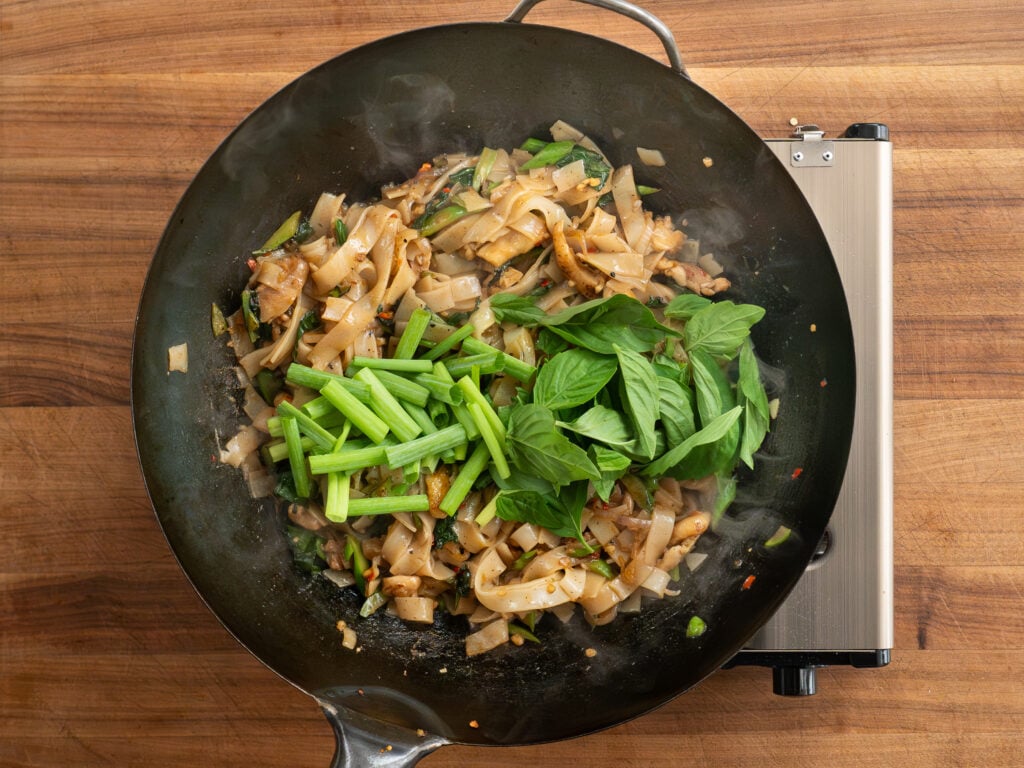 scallions and basil on top of drunken noodles in wok