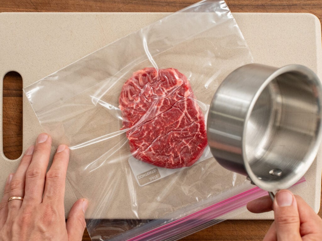 steak in plastic bag being pounded by sauce pan