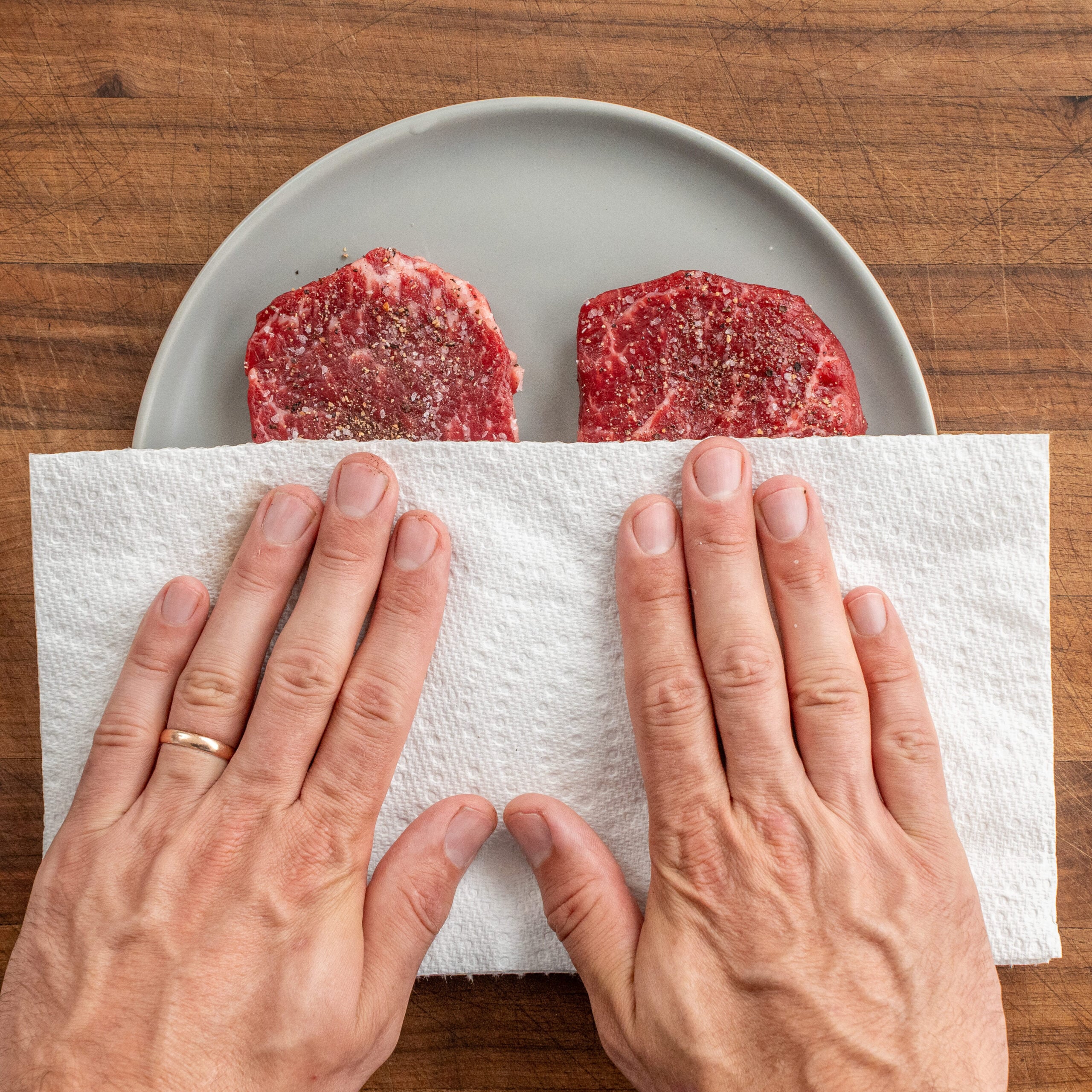 hands using paper towel to blog steak on grey plate