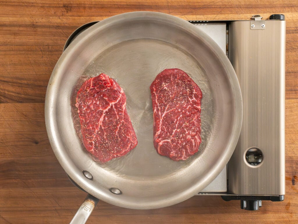 two raw steaks in silver saute pan