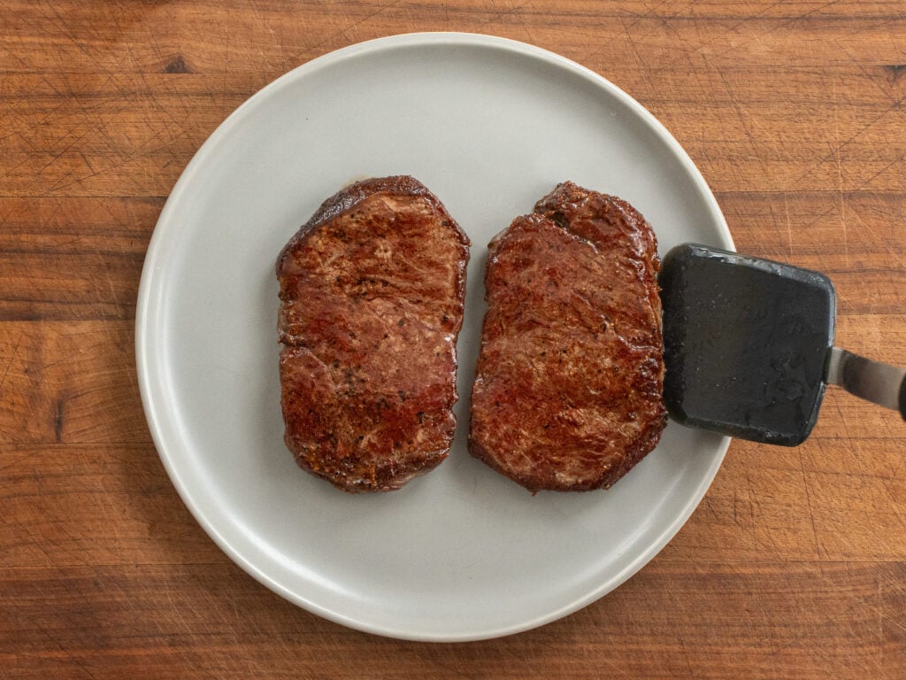 black spatula placing a seared steak on grey plate