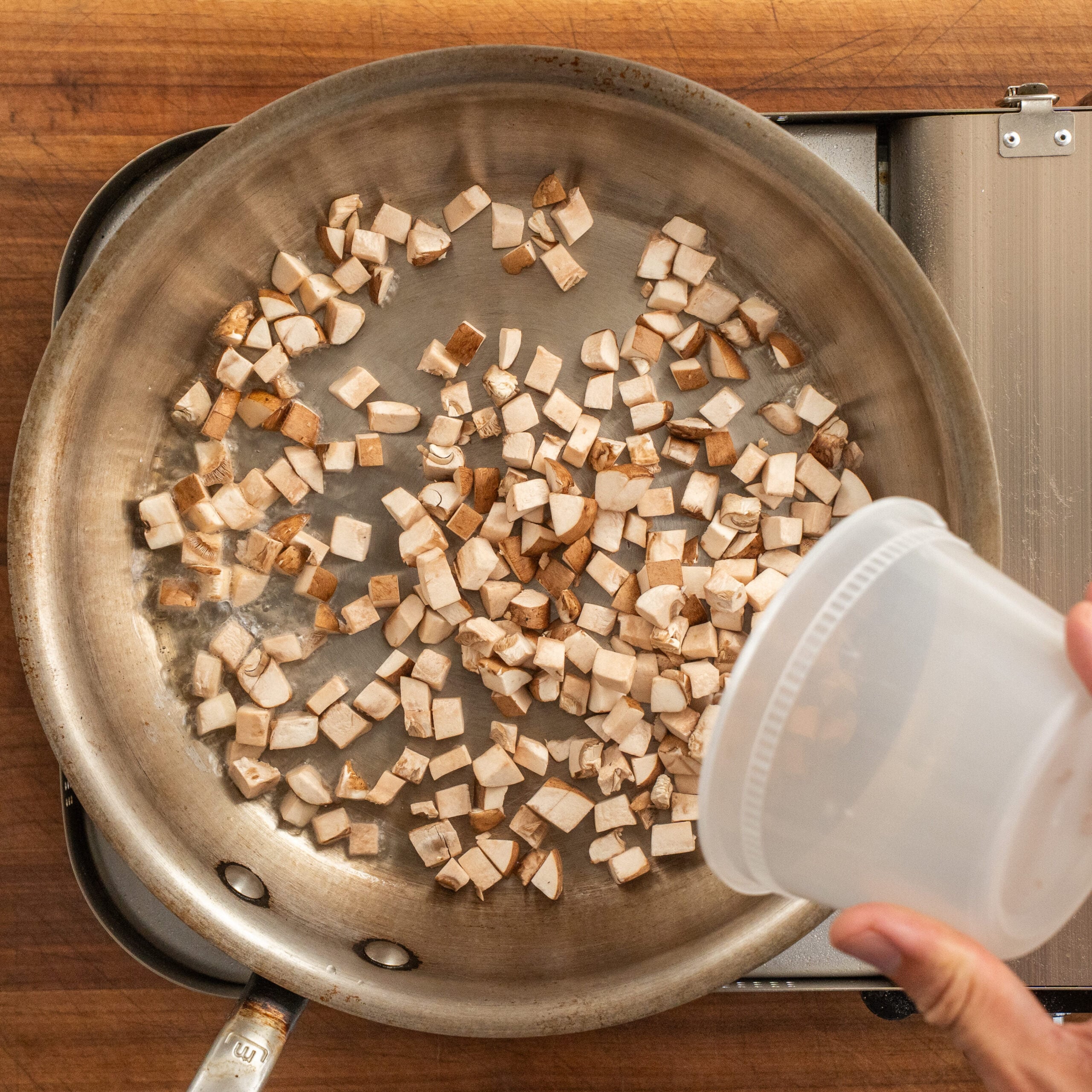 adding container or diced mushrooms to silver saute pan