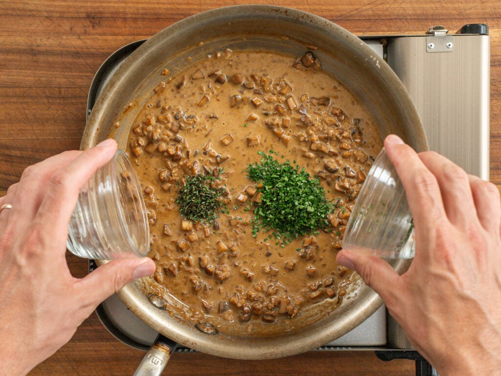 adding clear containers of thyme and parsley to finished steak diane sauce in saute pan