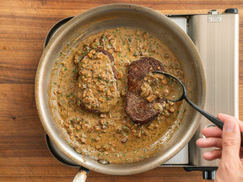 basting seared steaks in steak diane sauce with black spoon