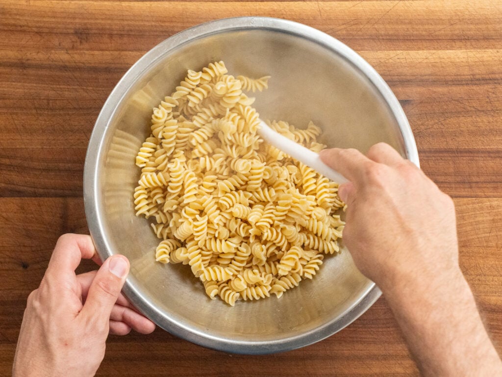 stirring cooked fusilli pasta with white spatula