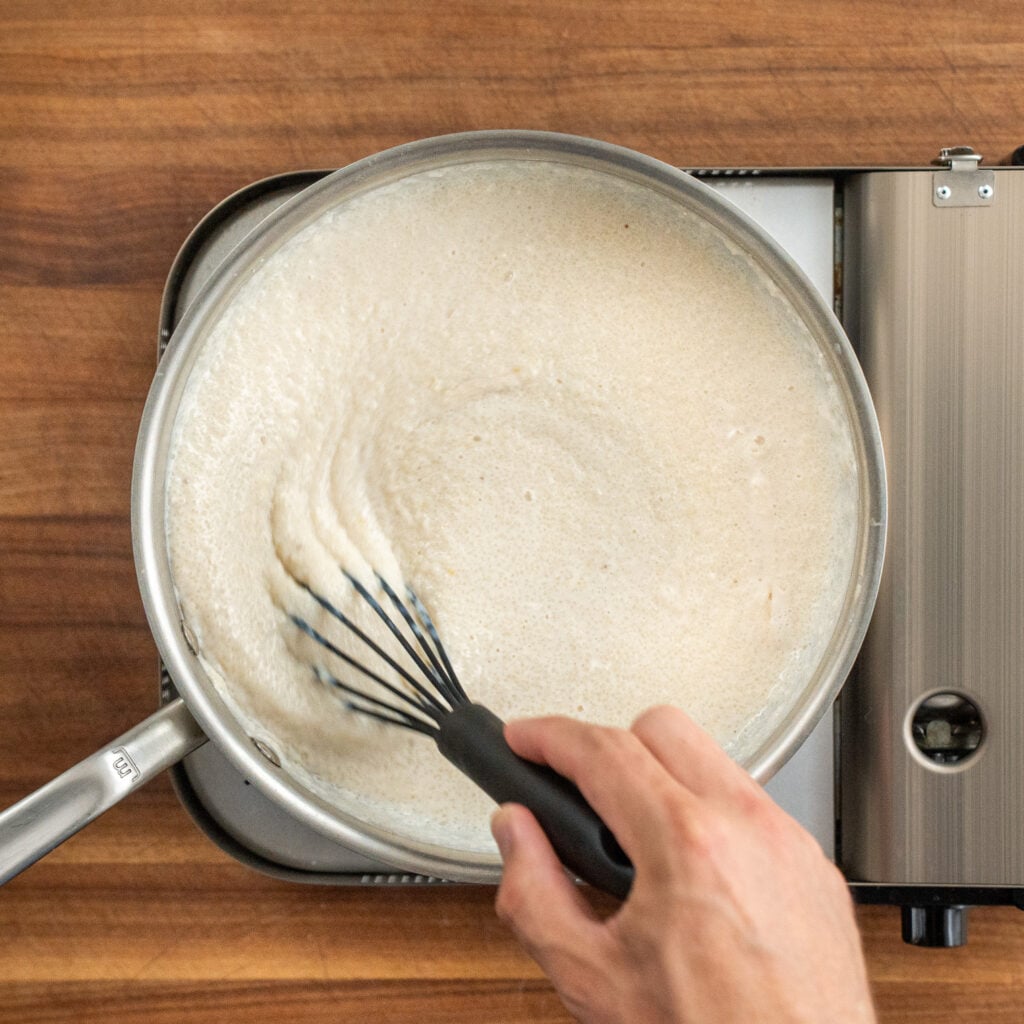 black whisk stirring grits in silver sauce pot