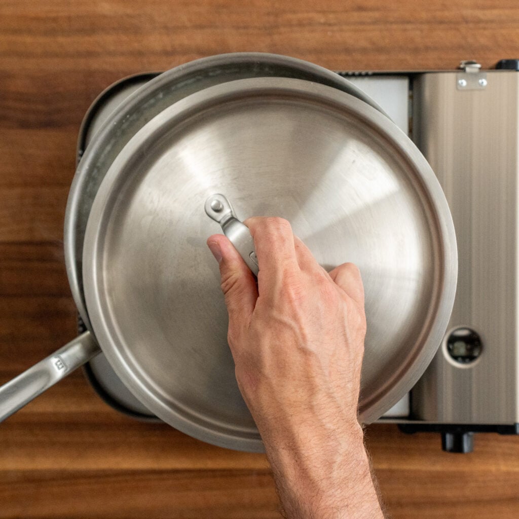 hand placing lid on silver sauce pot