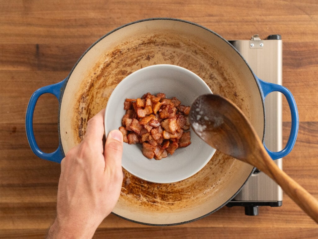 wooden spoon placing cooked bacon into grey bowl