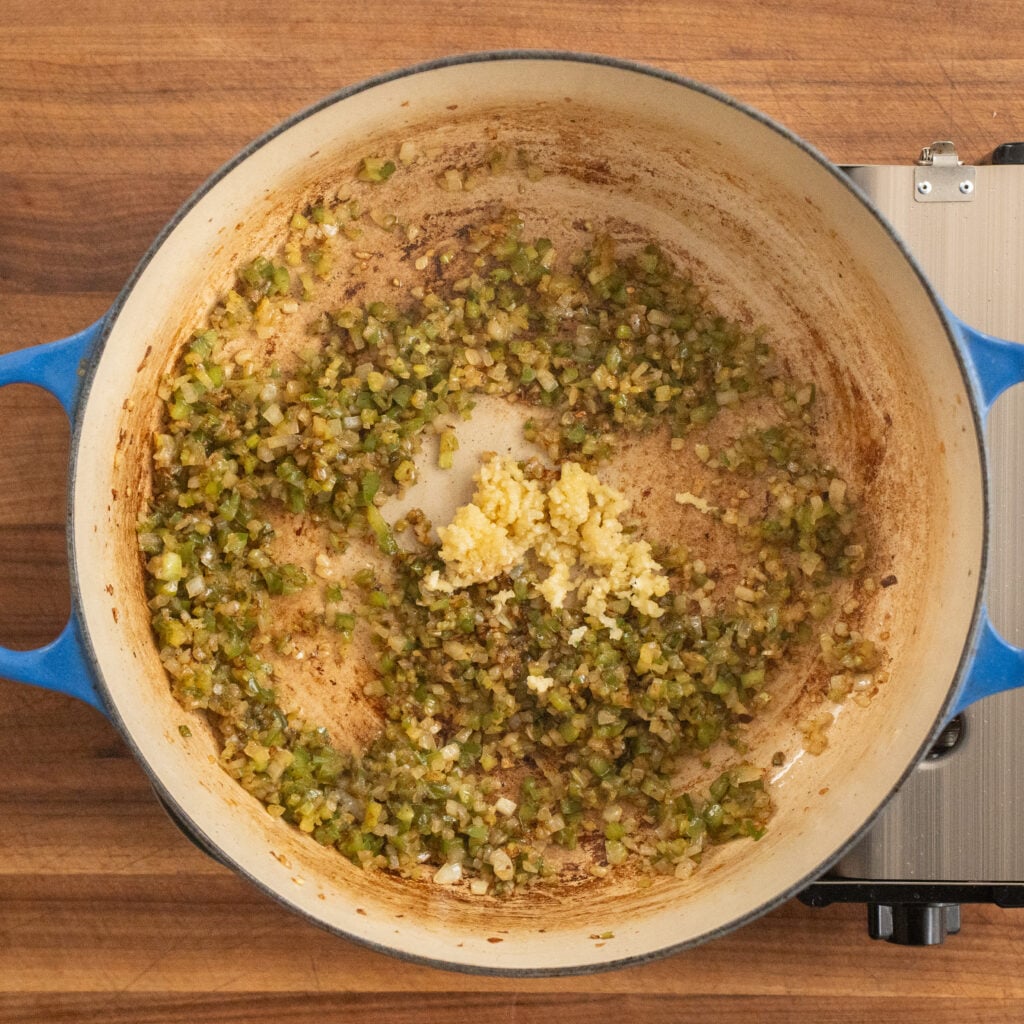 minced garlic sitting on top of cooked trinity in dutch oven