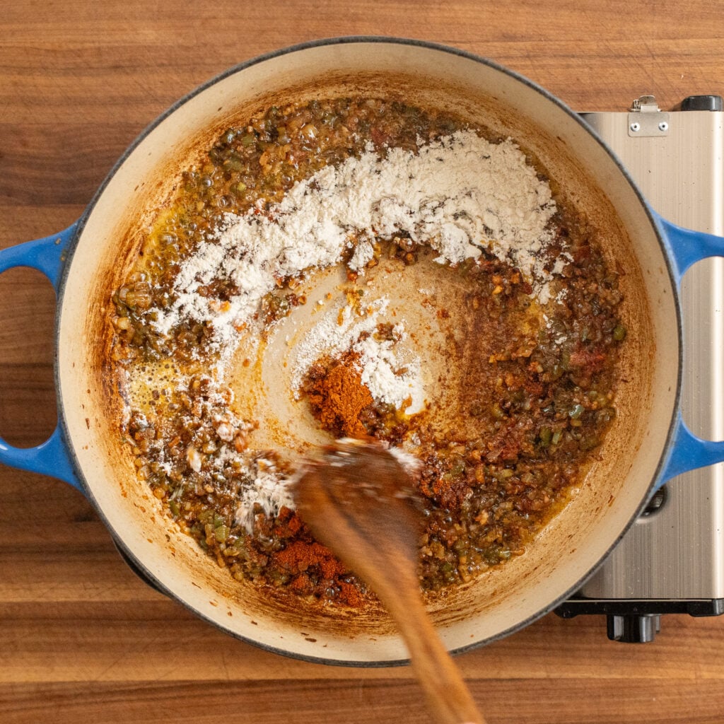 wooden spoon stirring flour into cooked vegetables and bacon mixture