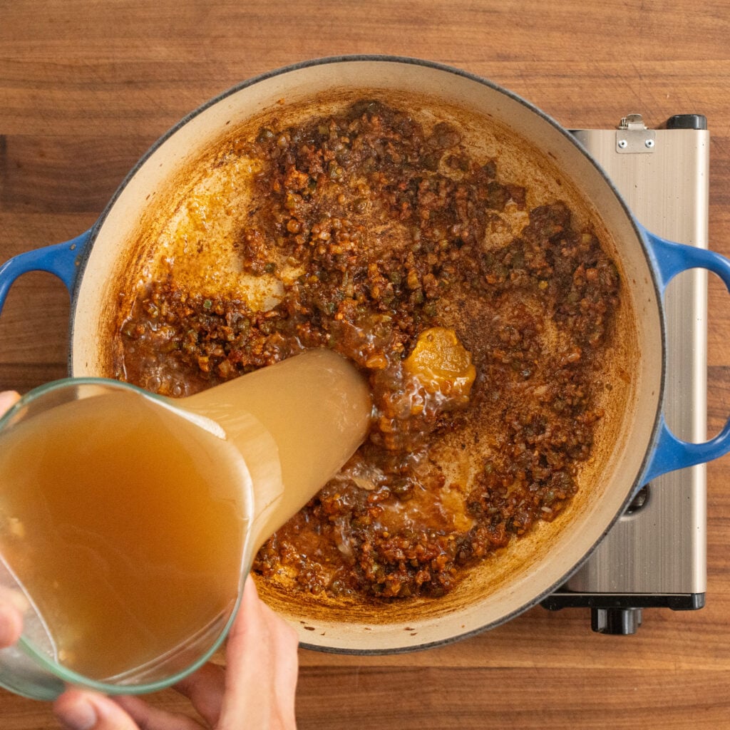 pouring brown liquid into orange vegetables and bacon mixture
