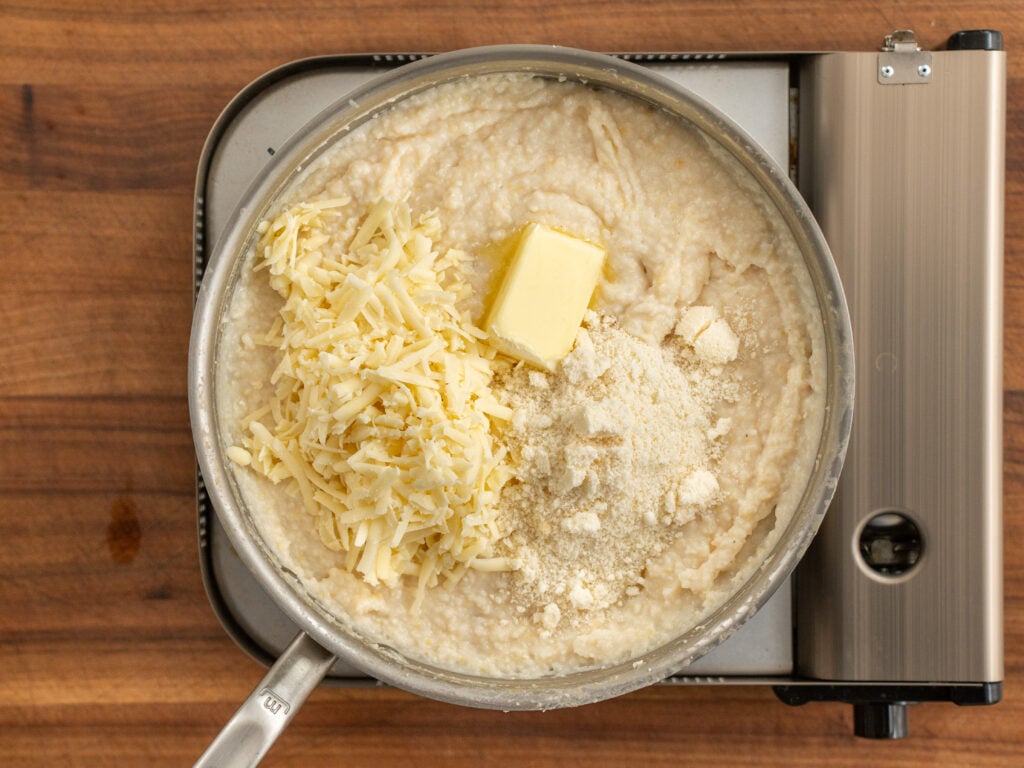 sauce pan of grits topped with shredded cheese and butter