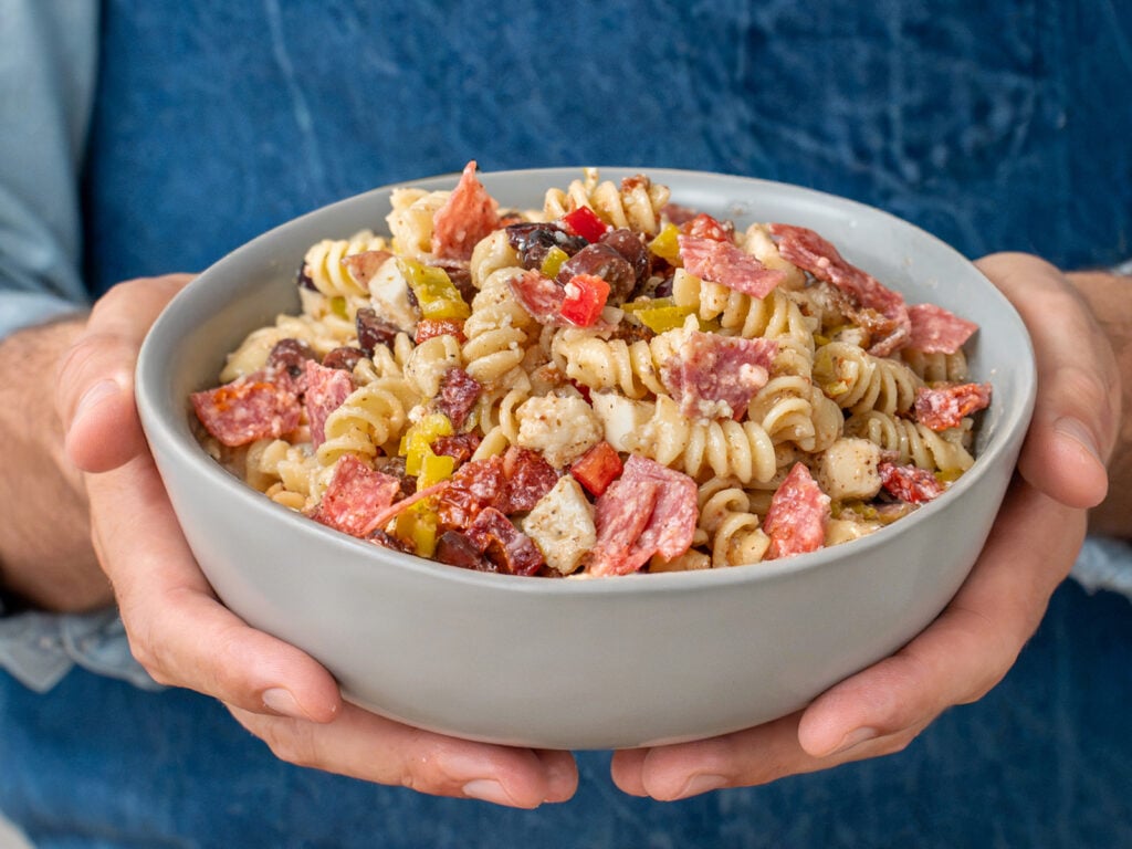 man holding grey bowl filled with Italian pasta salad