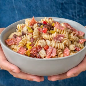 man holding grey bowl filled with Italian pasta salad