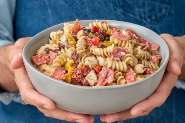 man holding grey bowl filled with Italian pasta salad