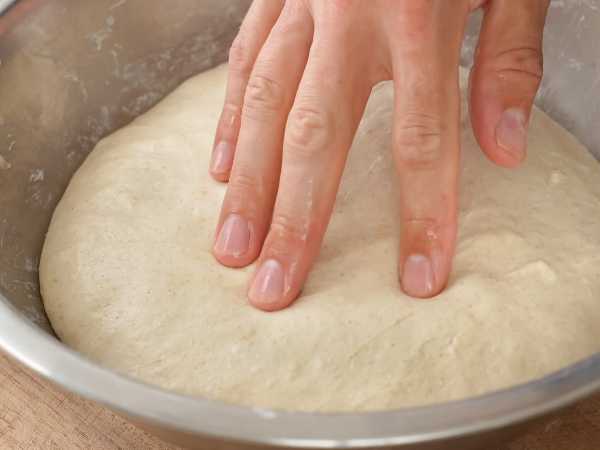 hand poking proofed sourdough in metal bowl