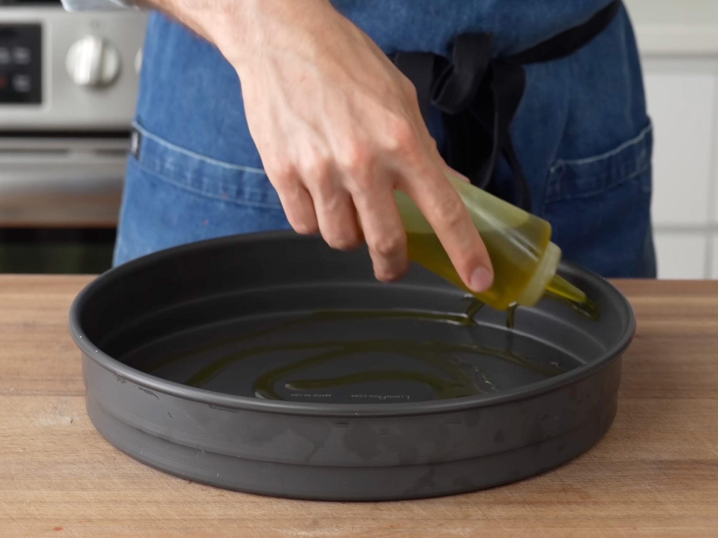 using a squeeze bottle to oil inside of a round high sided metal pizza pan