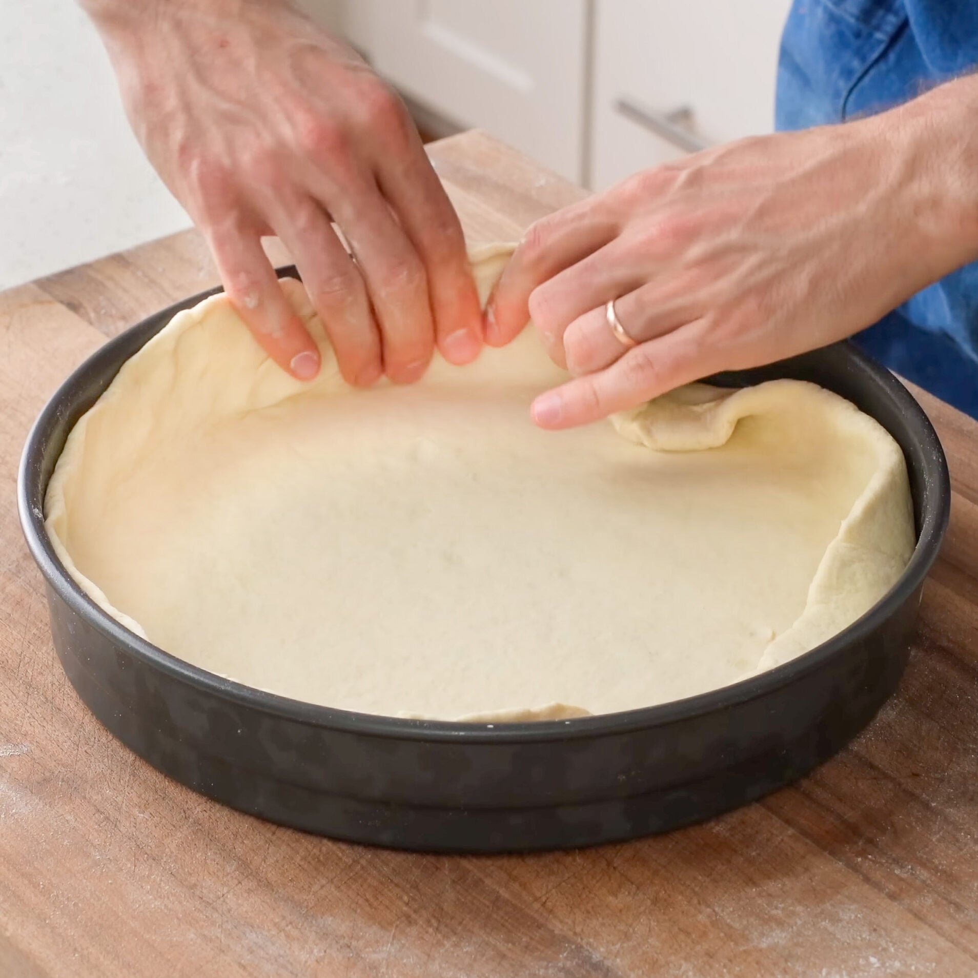 hands pressing deep dish pizza dough into metal pan