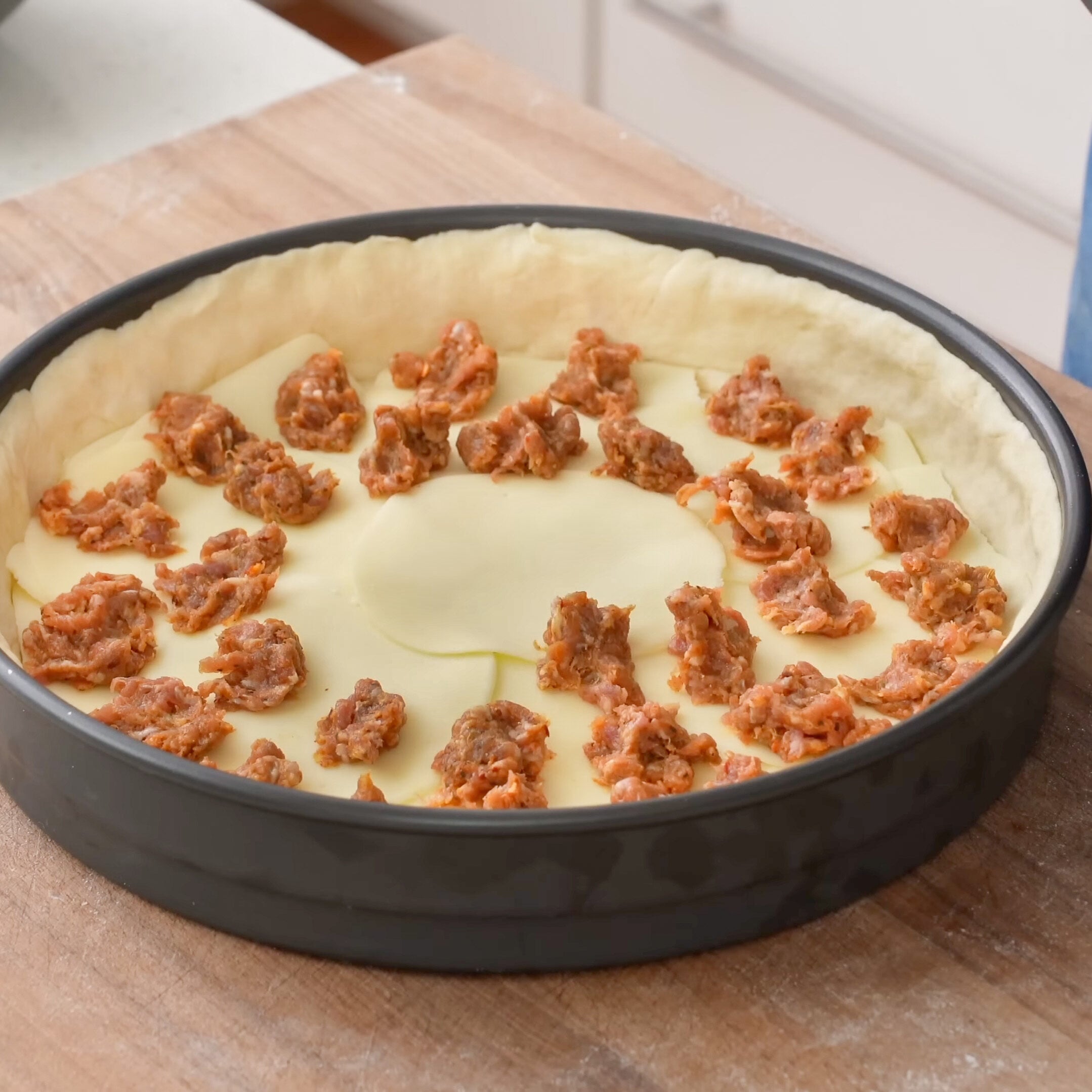 deep dish pizza dough formed in round pan with small rounds of Italian saucage placed on the bottom