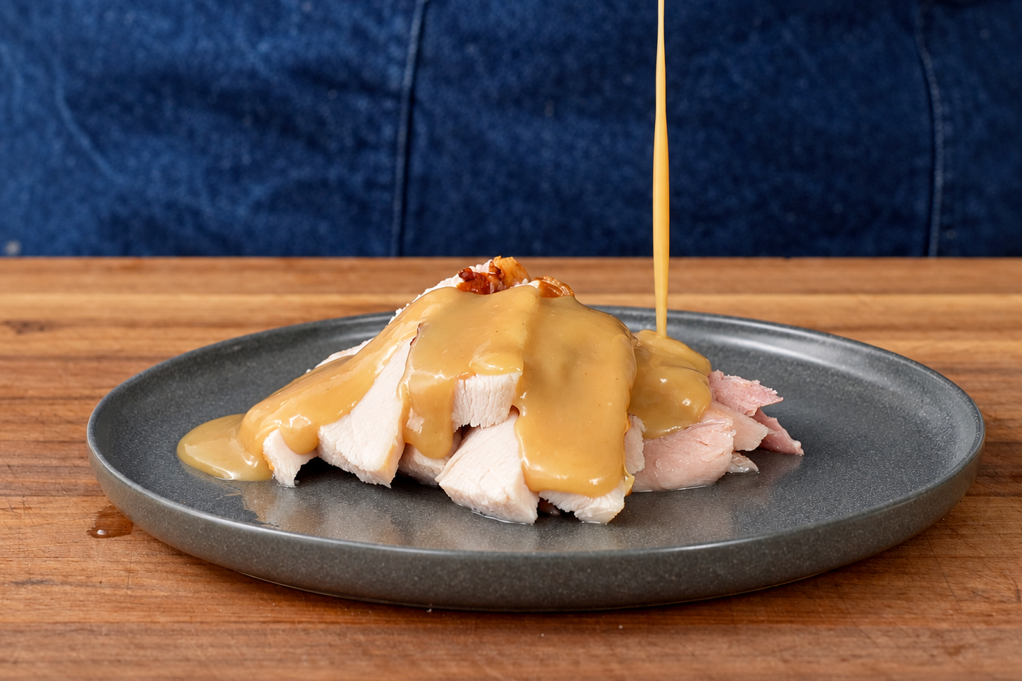 gravy dripping onto grey plate filled with slices of roast turkey