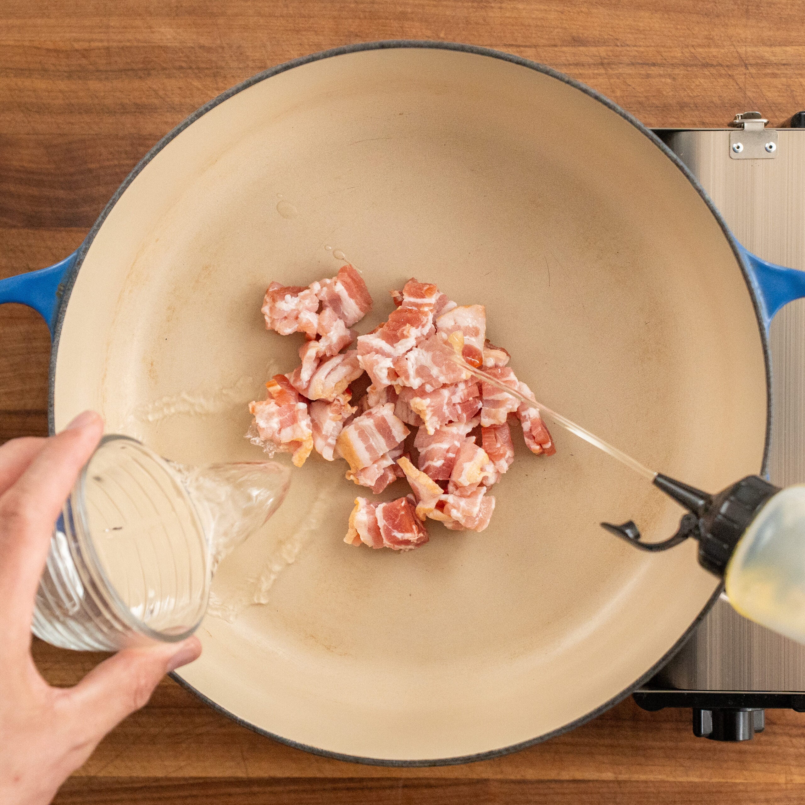 adding water and oil into dutch oven filled with a small pile of raw bacon