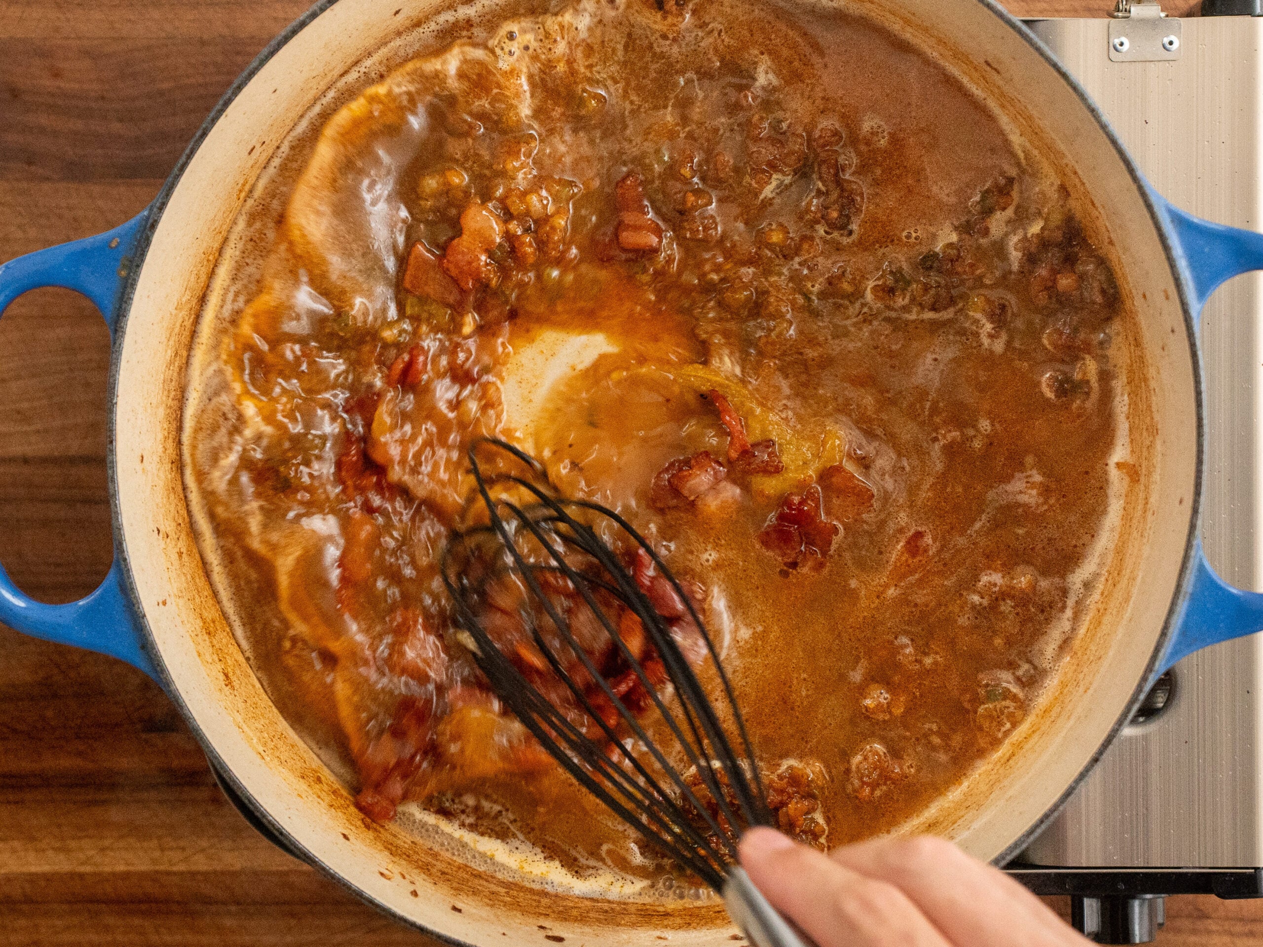 black whisk stirring bacon gravy in blue dutch oven
