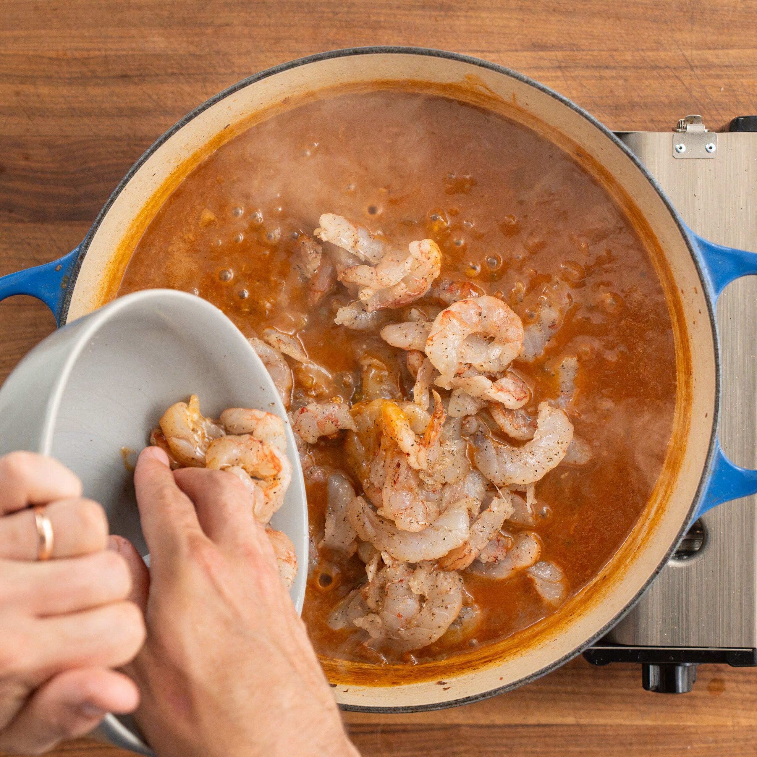adding grey bowl filled with shrimp into bubbling orange sauce