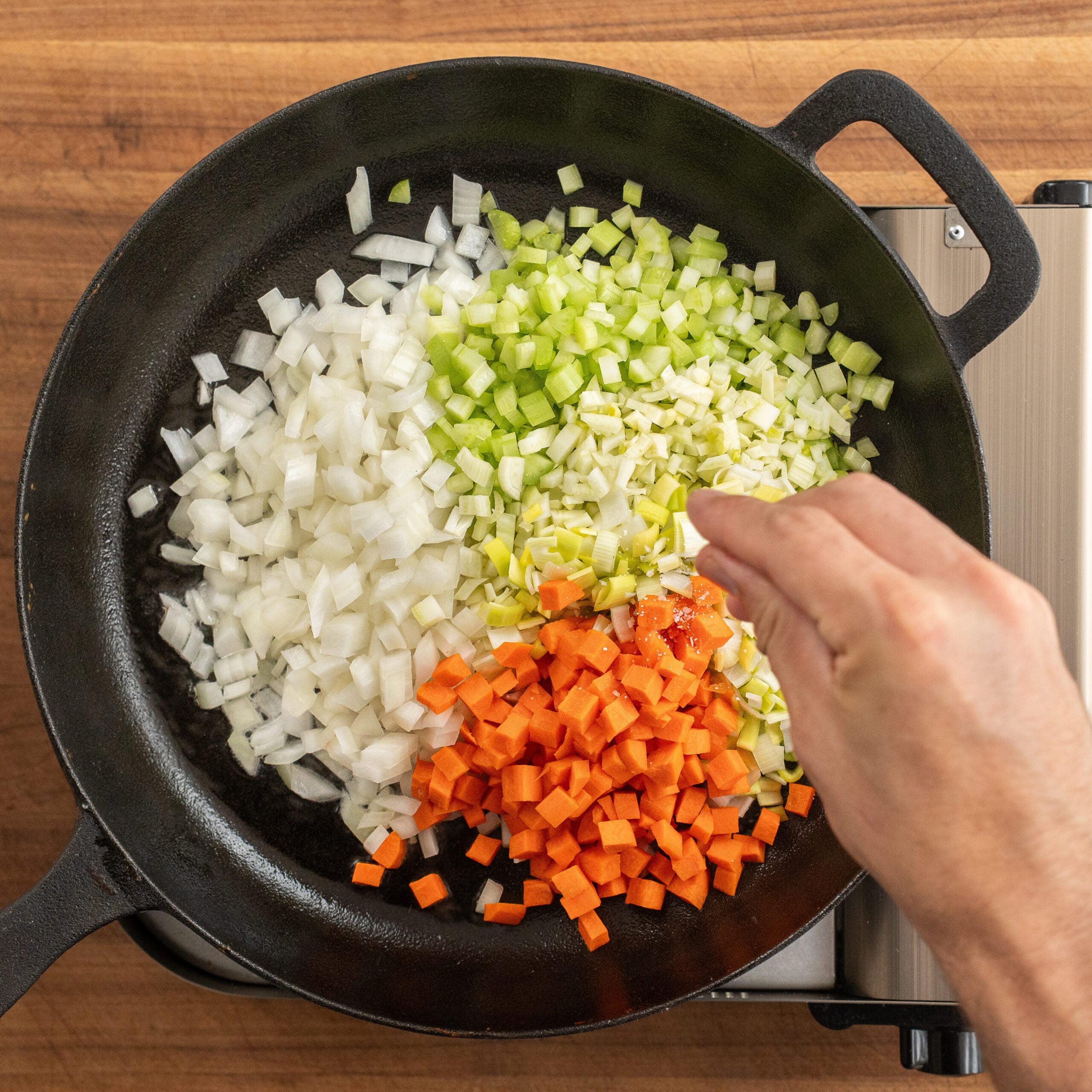 adding pinch of salt to leek fennel celery carrot in black cast iron pan