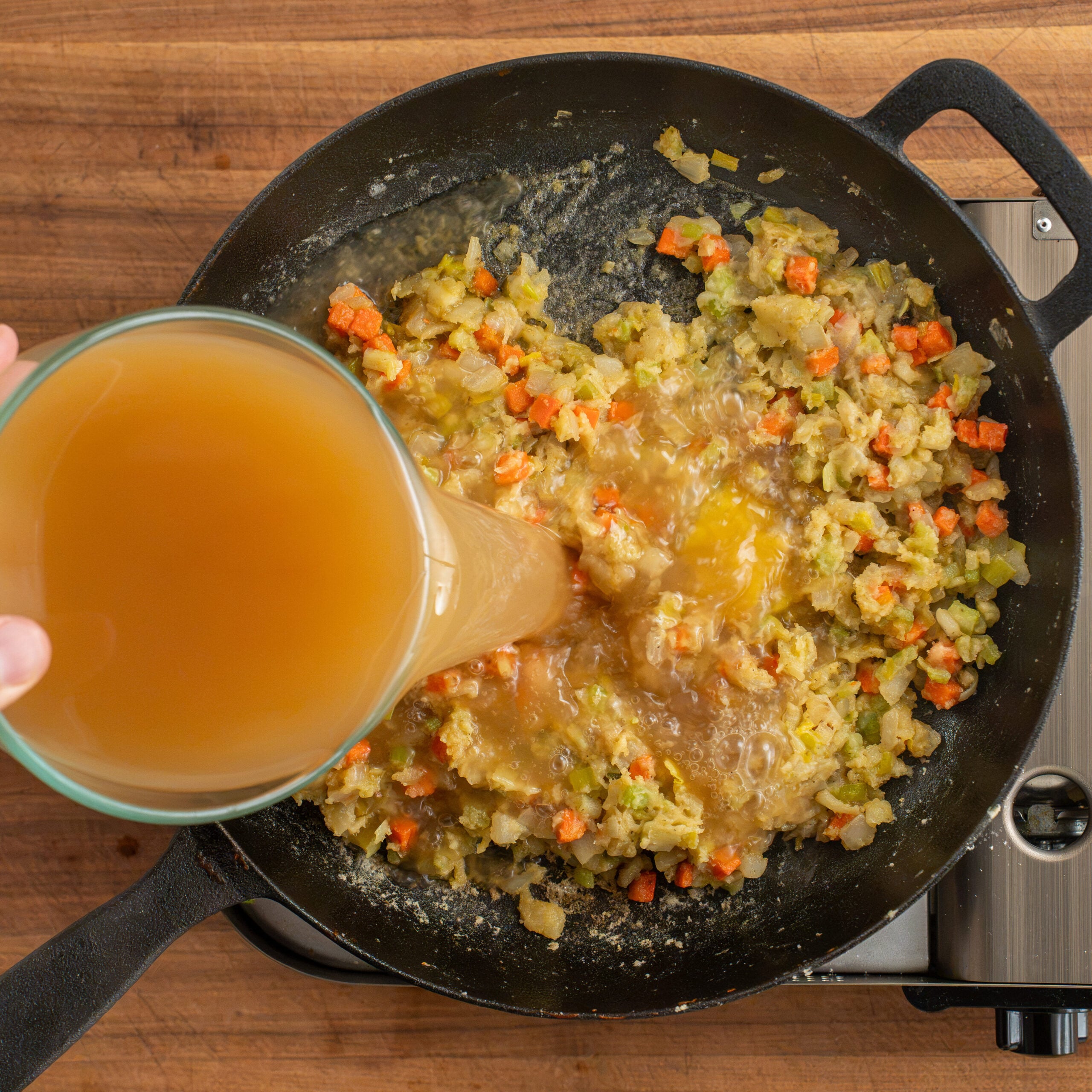 adding chicken stock to vegetables in black cast iron pan