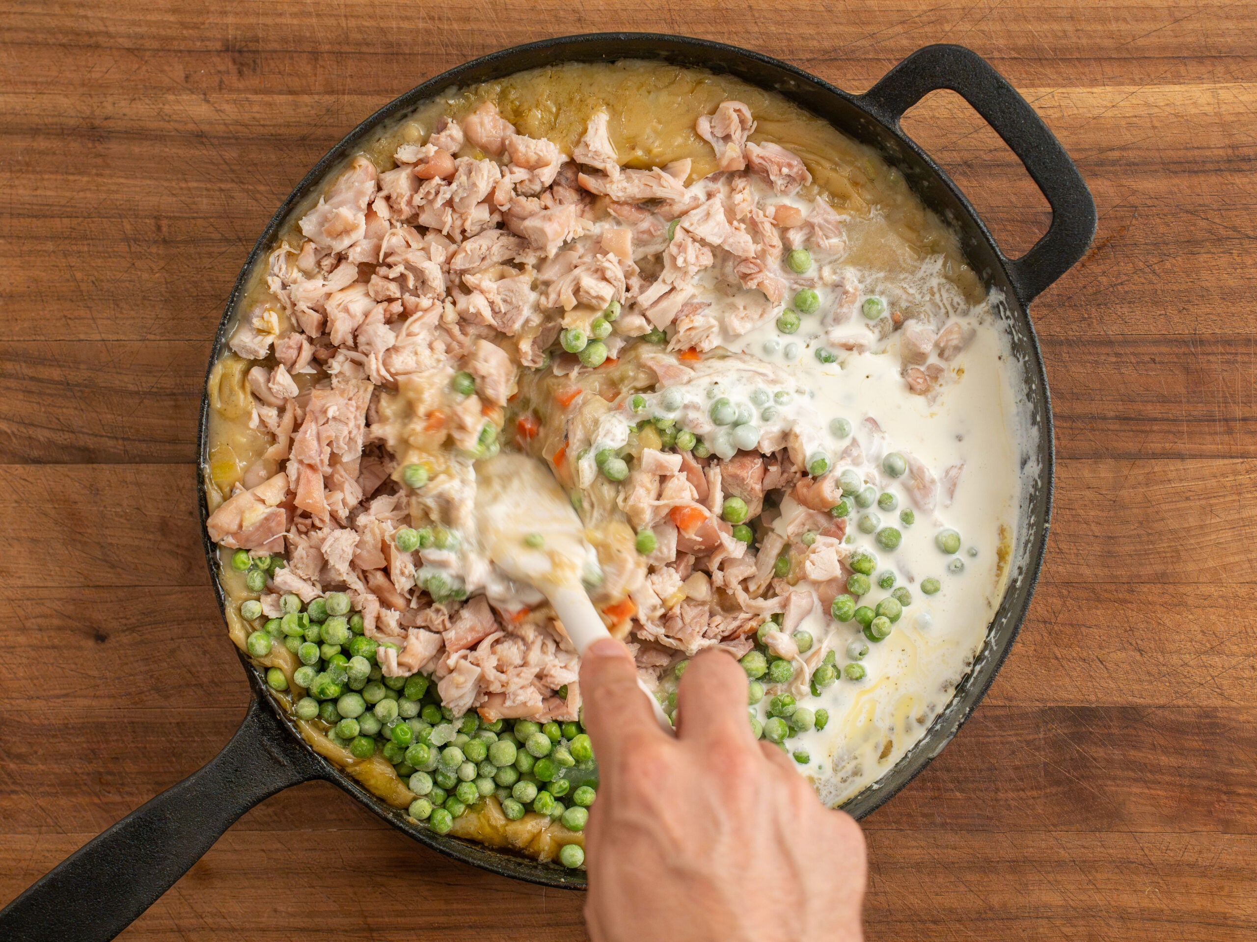 stirring chicken peas and cream into chicken pot pie filling in cast iron pan