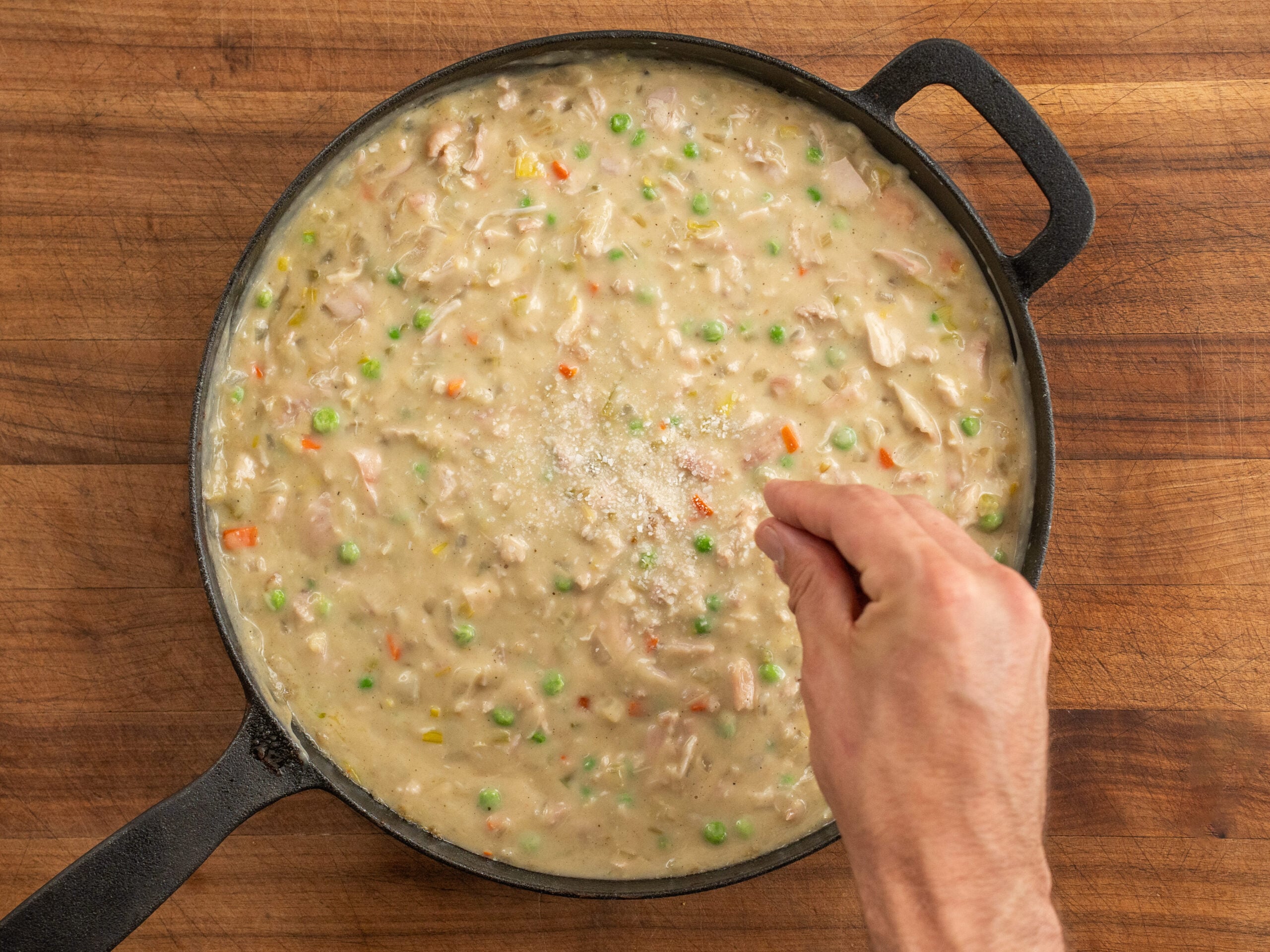 adding pinch of salt into chicken pot pie filling in black cast iron pan
