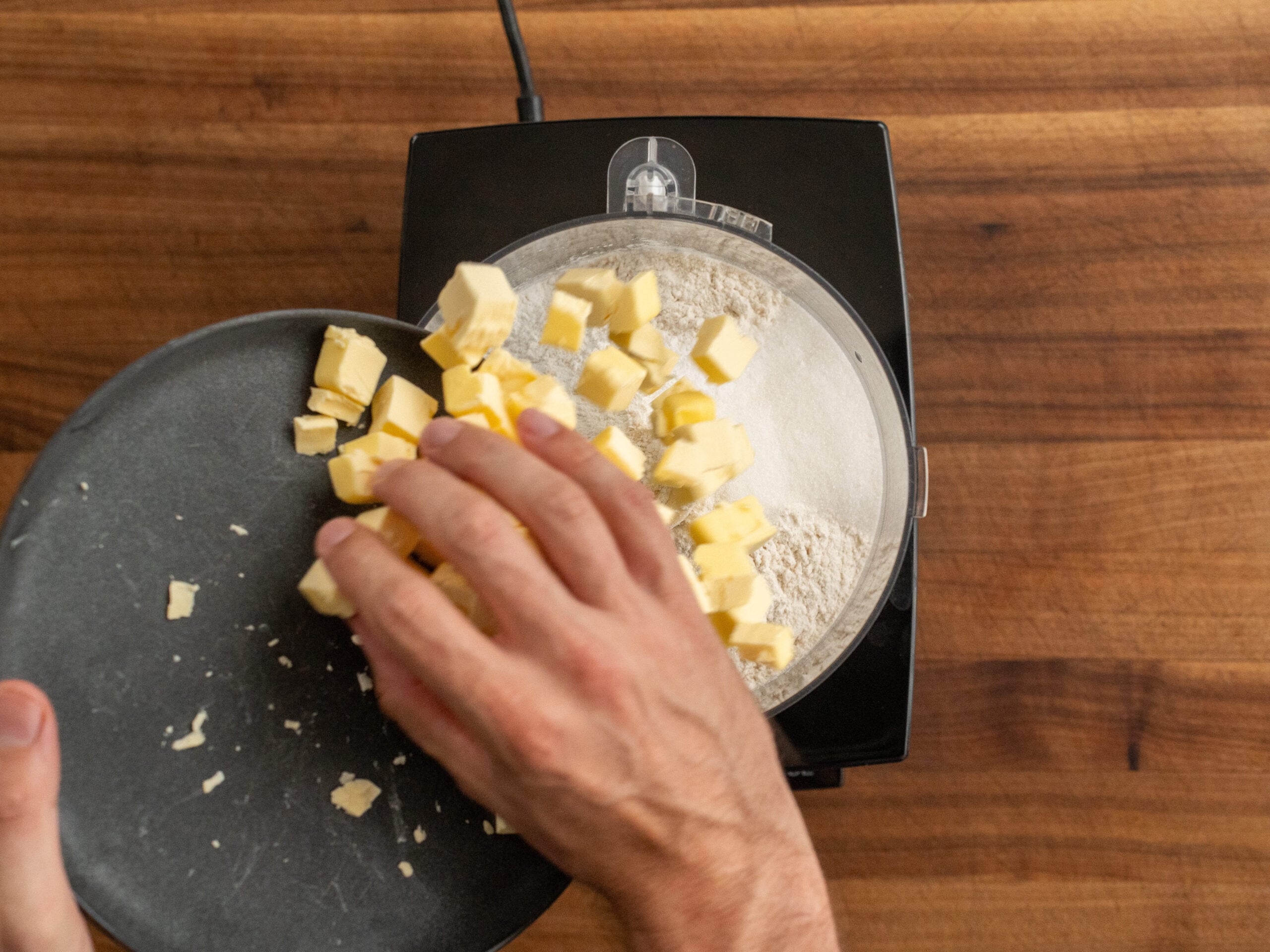 hand sliding cubed butter from black plate into food processor