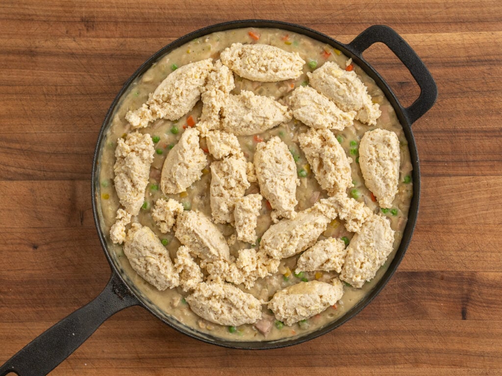 raw biscuit dough on top of chicken pot pie in black cast iron pan