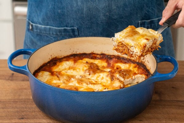 spatula lifting slice of lasagna out of blue dutch oven