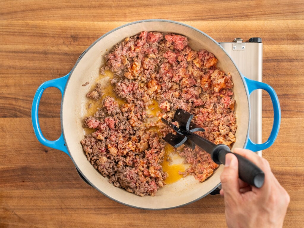 black meat chopper chopping up cooking ground beef and pork in blue dutch oven